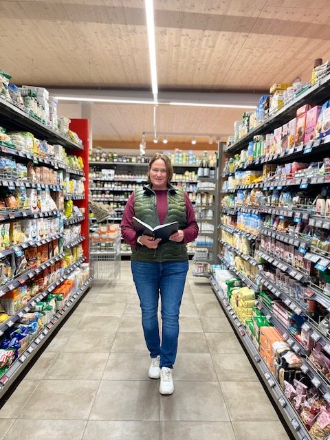 Barbara Fegerl geht mit Notizbuch durch einen Supermarktgang